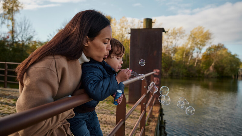 Mutter mit Kind, das Seifenblasen pustet, am Ufer