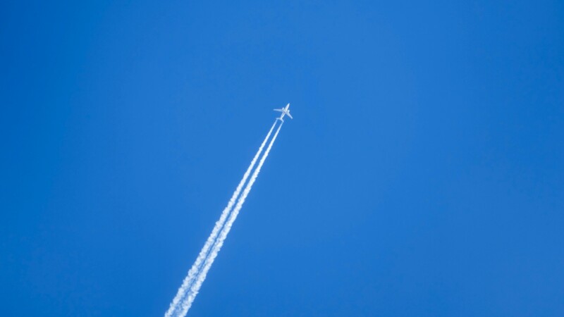 Flugzeug mit Kondensstreifen vor blauem Himmel