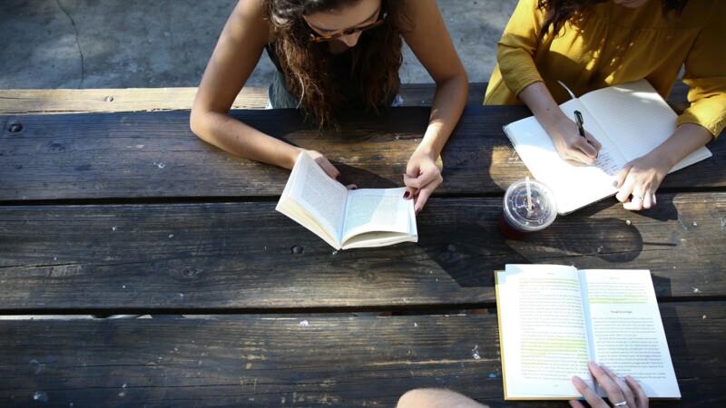 Drei junge Menschen sitzen an einem Tisch im Freien und lesen und schreiben